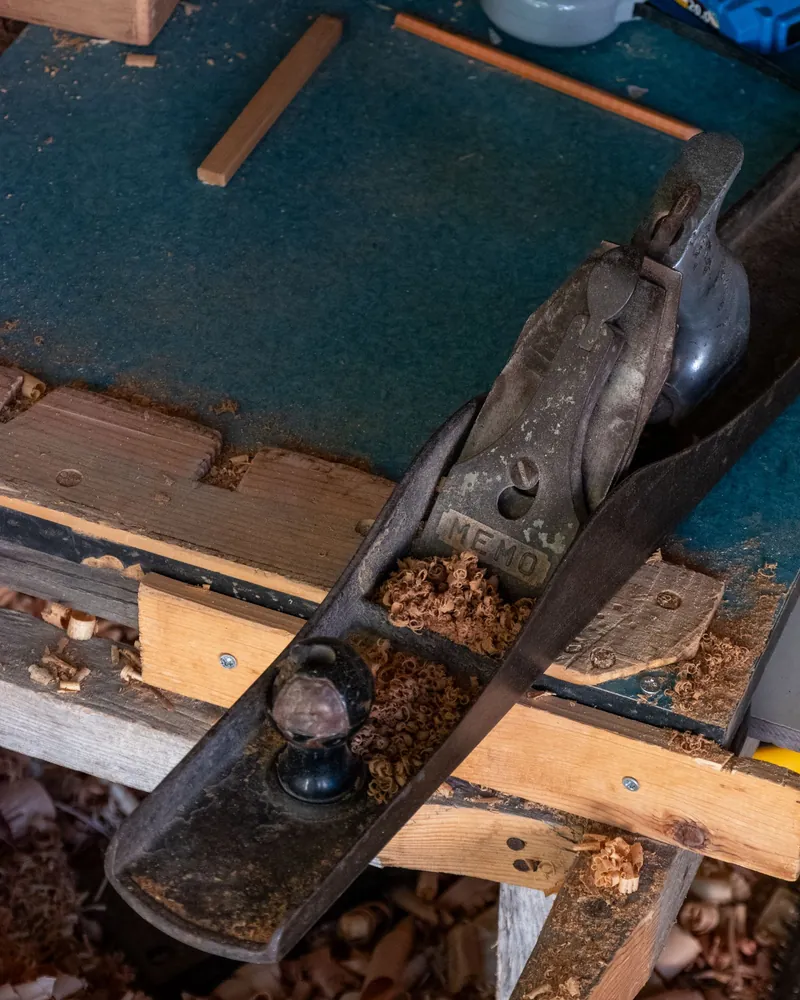 Cepillo de banco metálico apoyado sobre un banco de carpintero entre virutas rizadas de madera